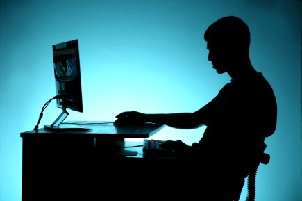 Black silhouette of teenager sitting at the computer on blue bac